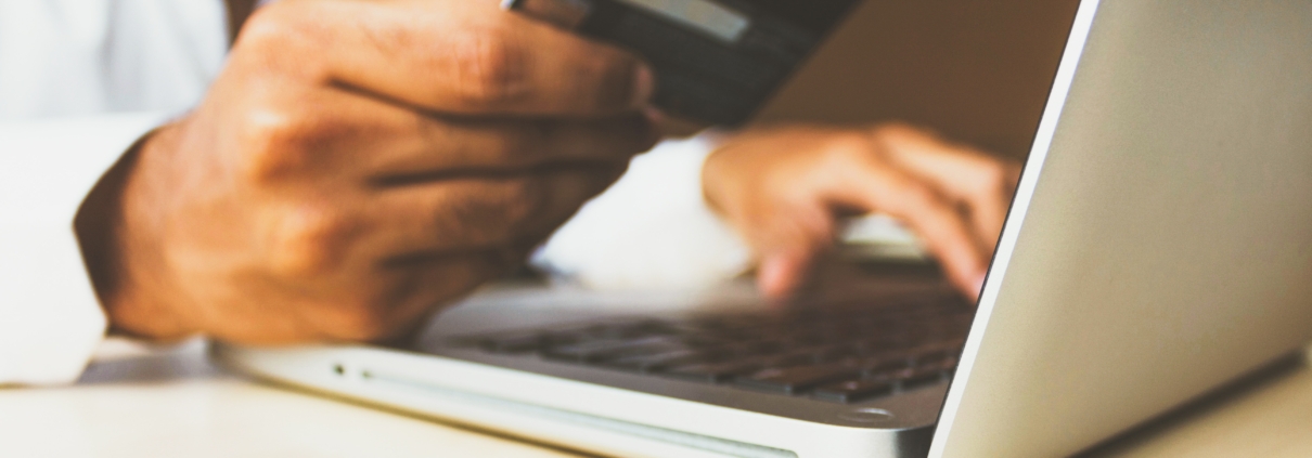 Person paying bills online using a computer and bank card, emphasizing Telecom Billing efficiency.